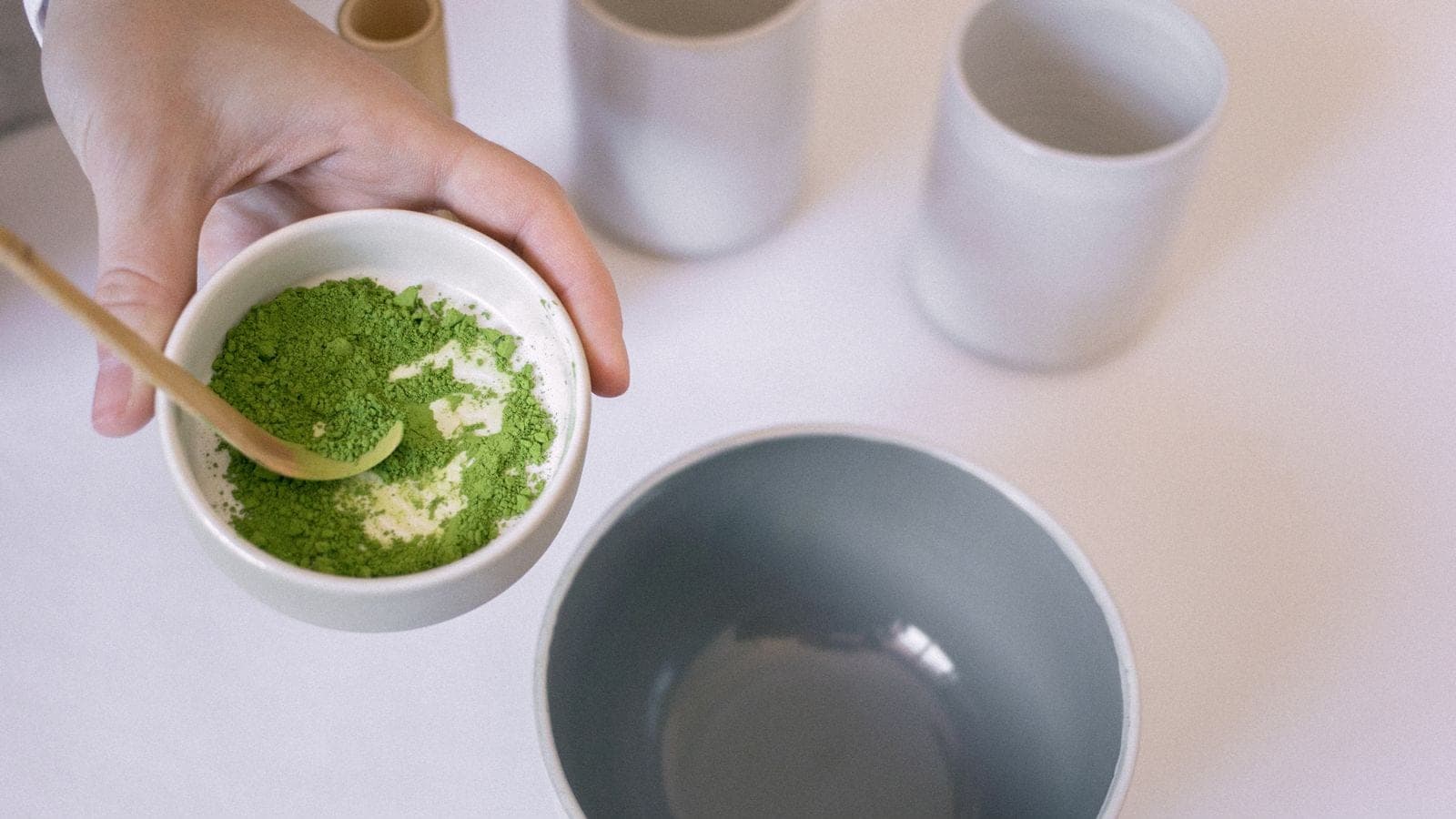A hand holding a small bowl of bright green matcha powder with a bamboo scoop