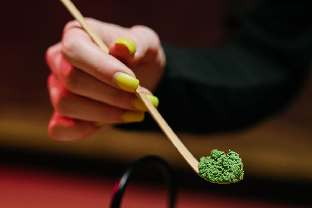 A bamboo scoop holding a small mound of vivid green matcha powder