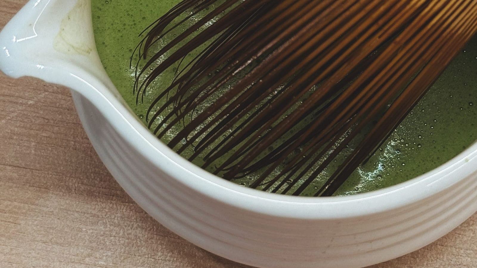 A bamboo whisk resting in a spouted bowl of freshly whisked green matcha