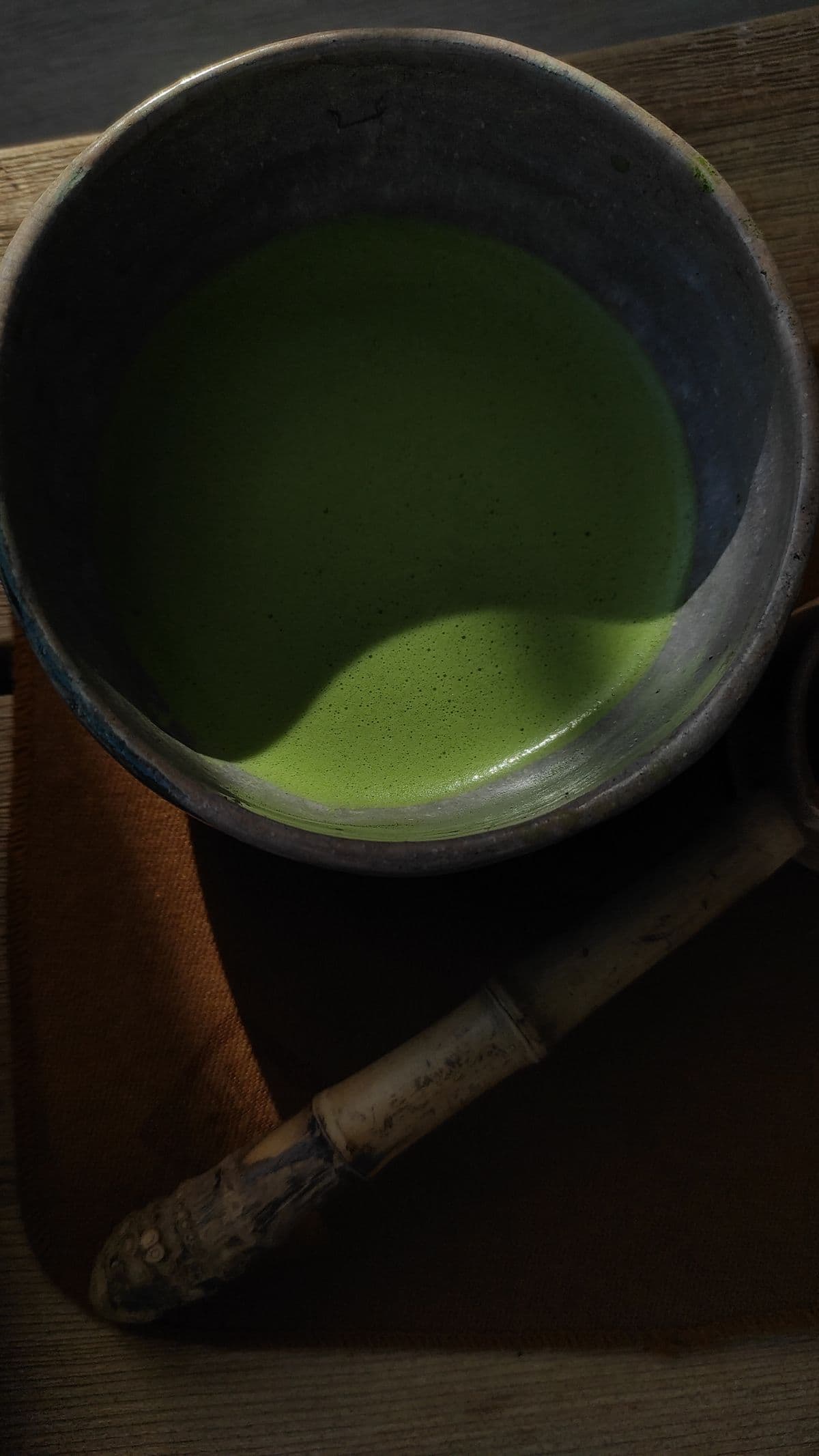 A bowl of freshly whisked matcha with a bamboo whisk resting against its rim