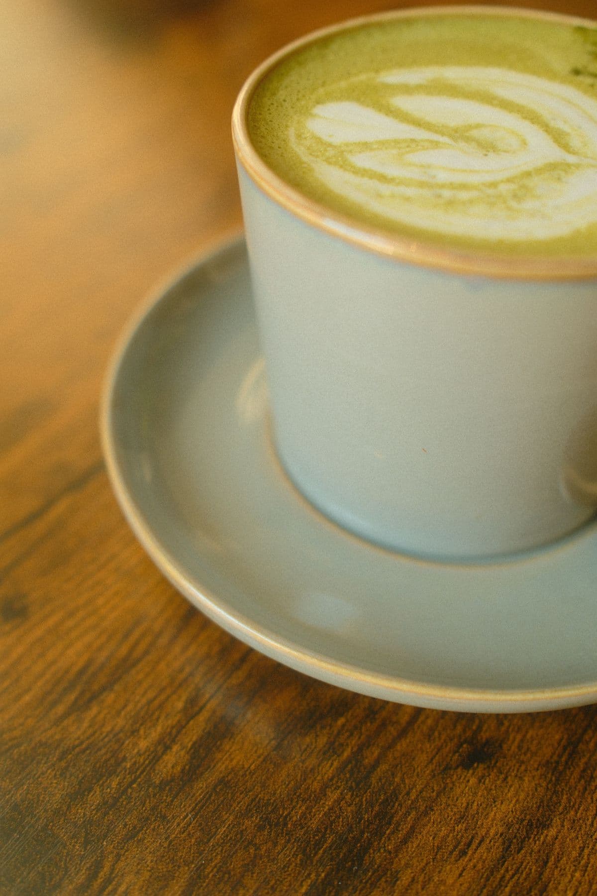 A matcha latte in a ceramic cup beside a bamboo whisk