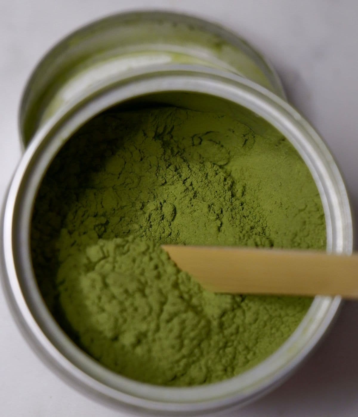 Green matcha powder in a tin with a bamboo scoop resting beside it