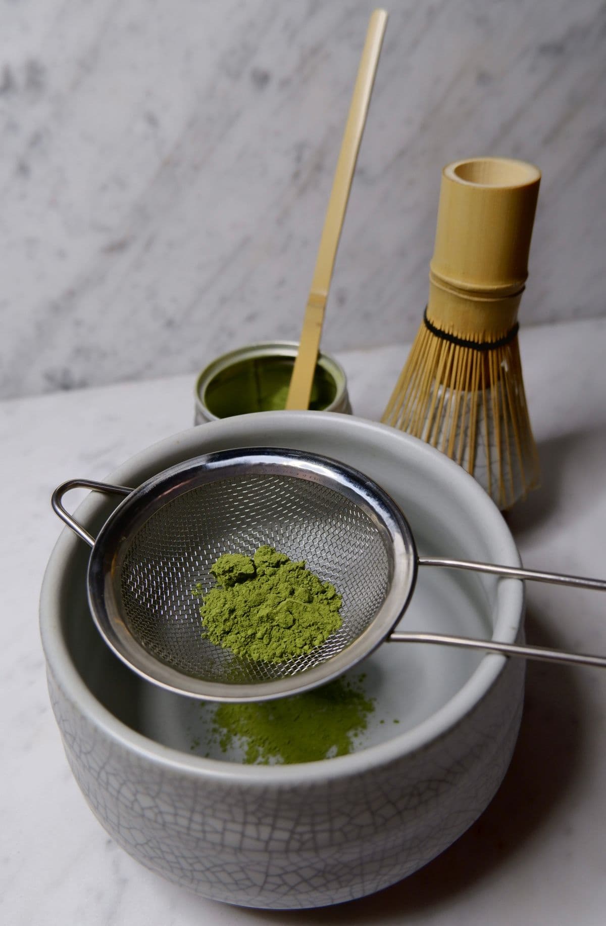 Matcha powder being sifted through a fine strainer into a bowl